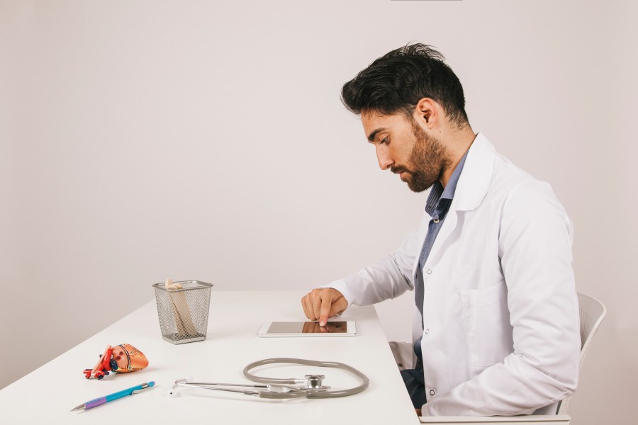 Andrologist in a white coat reviewing a tablet at a medical office desk with a stethoscope nearby